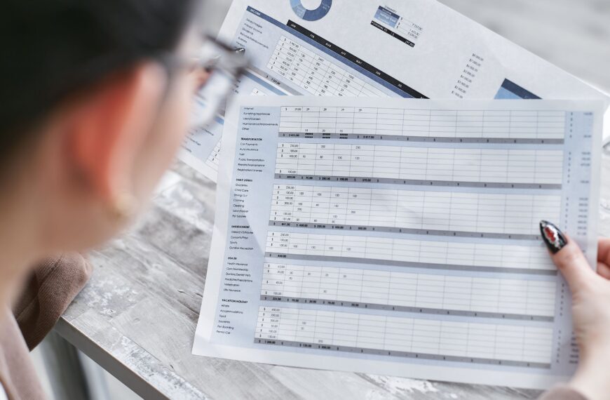 A businesswoman reviewing financial spreadsheets with charts and graphs in an office setting.